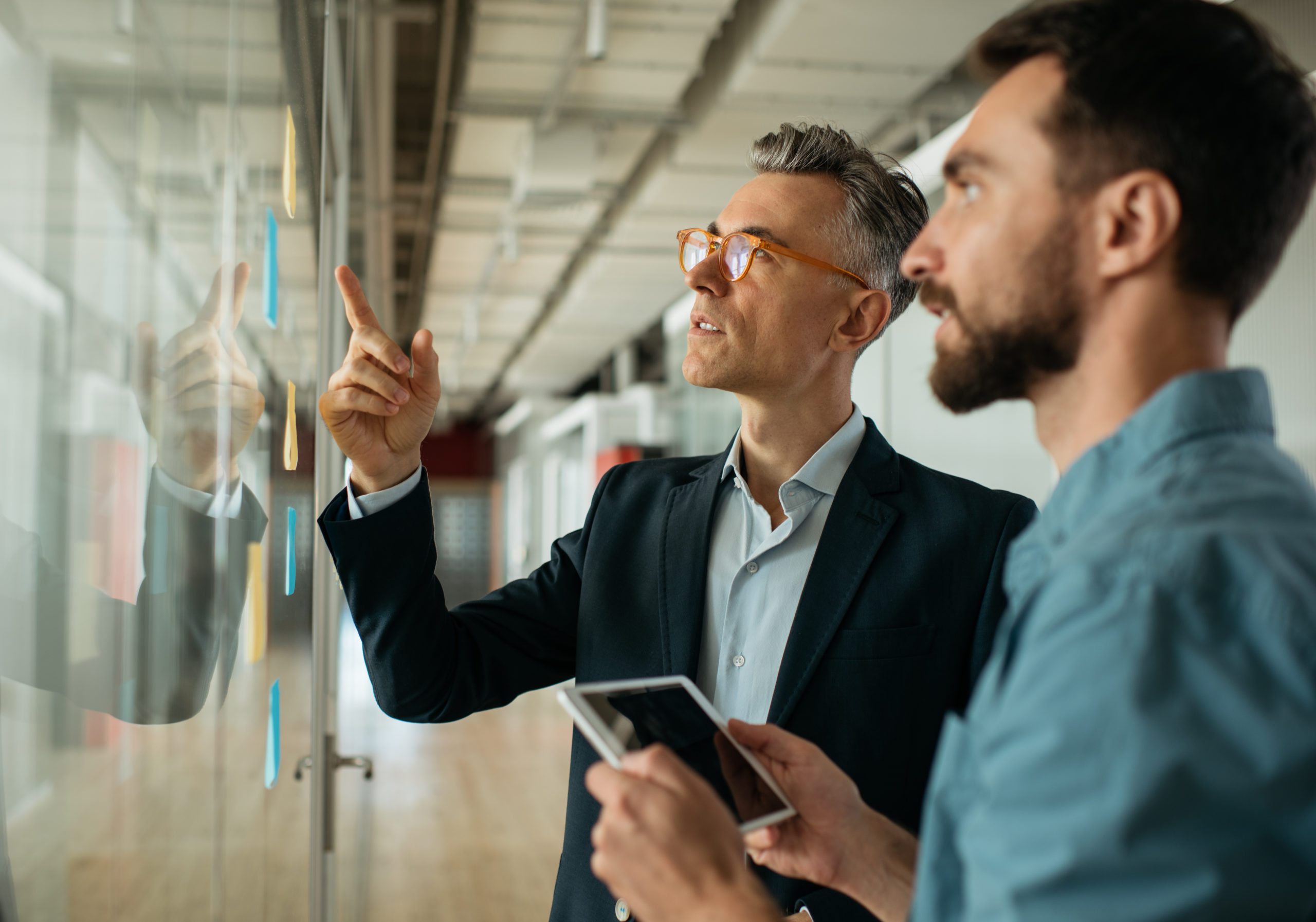 Business people meeting planning start up, talking, discussing ideas, brainstorming. Scrum master using sticky notes standing near planning board in modern office. Agile methodology, scrum concept okr-methodology